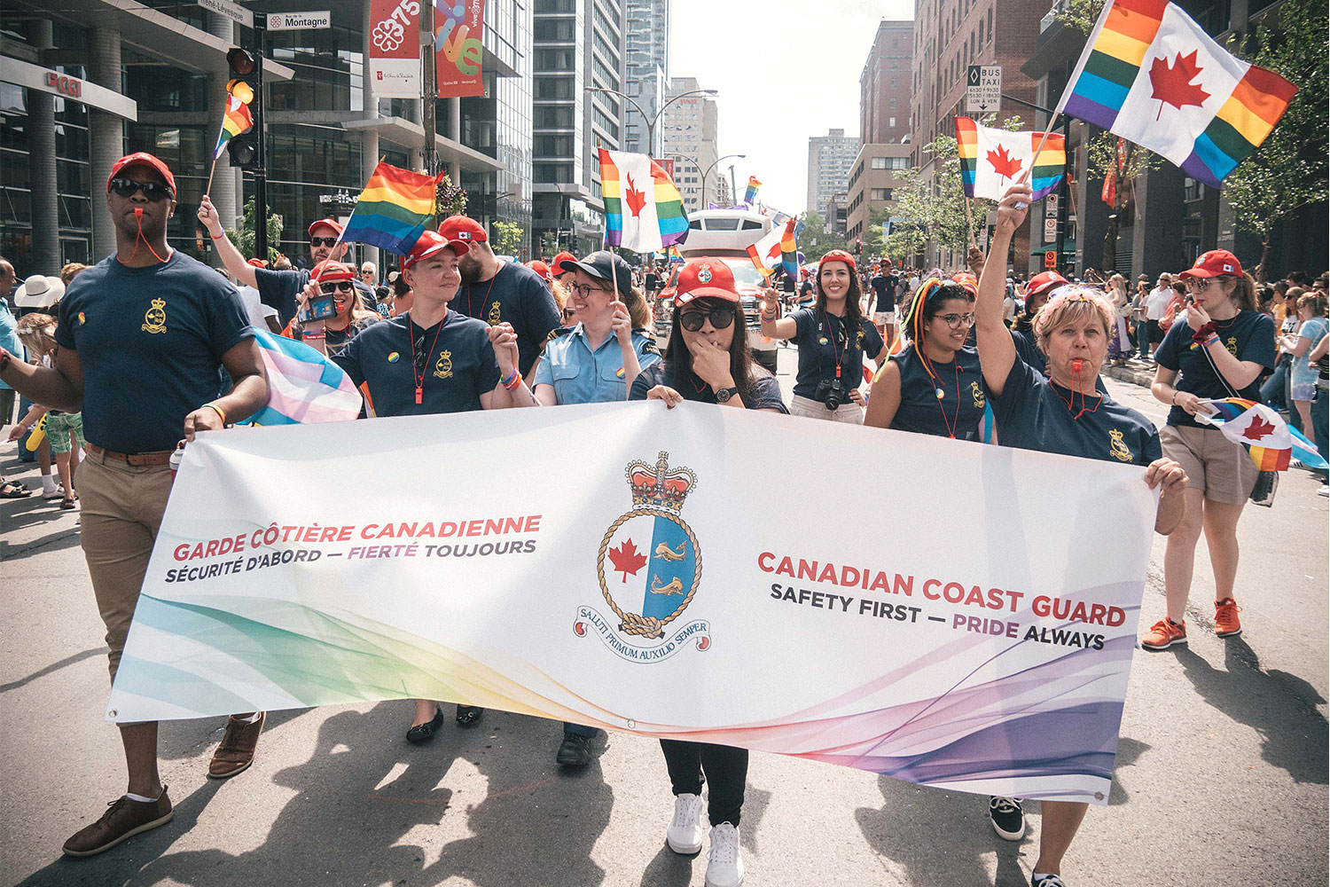 Photo de membres de la Garde côtière canadienne munis de drapeaux et d'une bannière, défilant dans les rues de Montréal