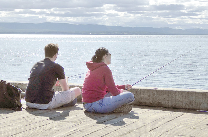 Un homme et une femme pêchent à la ligne assis sur le bord d’un quai.