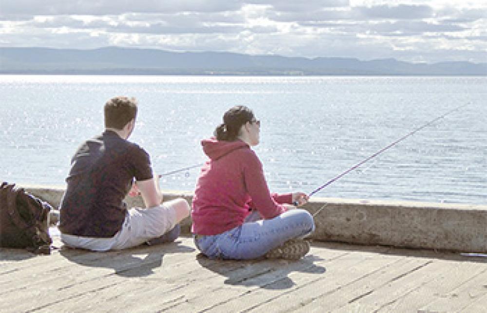 Un homme et une femme pêchent à la ligne assis sur le bord d’un quai.